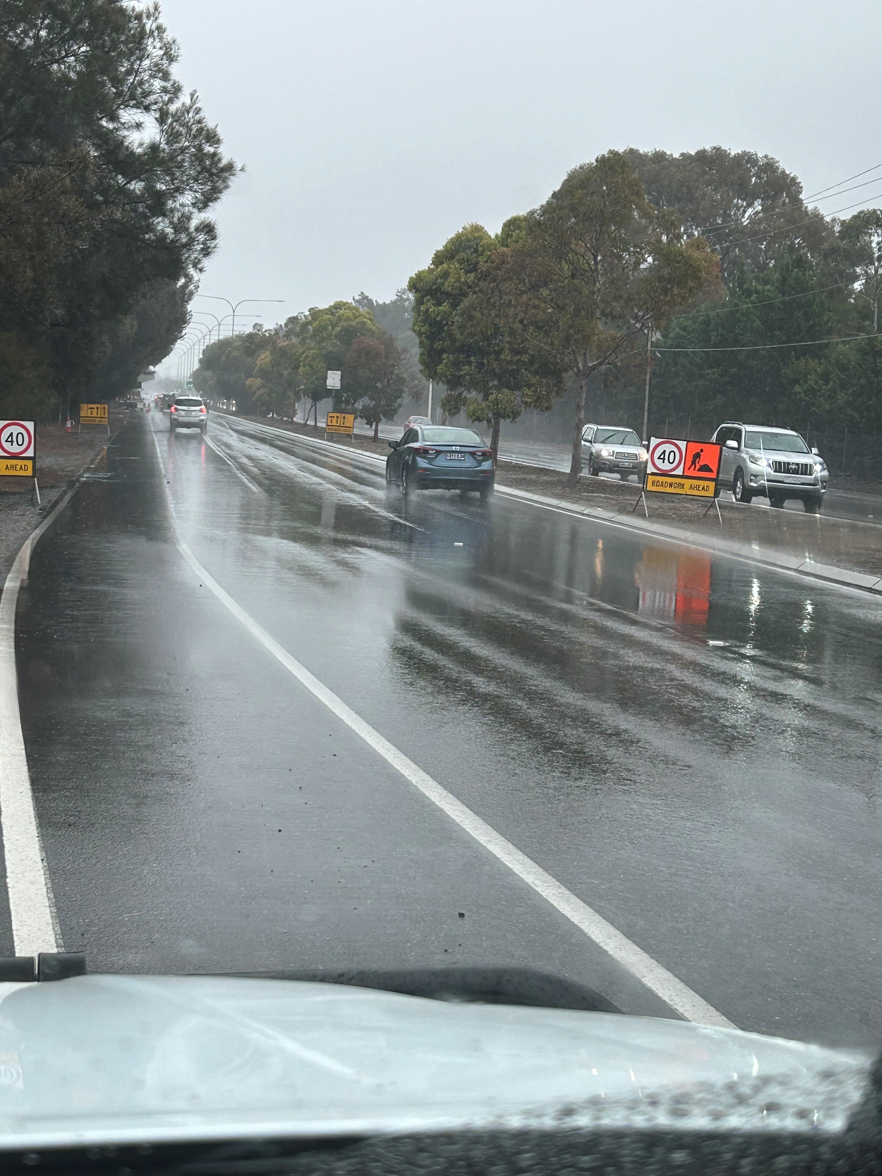 Traffic controllers managing a wet-weather roadwork zone on a busy highway